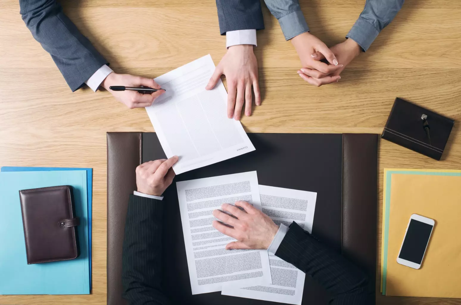 Business man and woman sitting at the lawyers's desk and signing important documents, hands top view, unrecognizable people